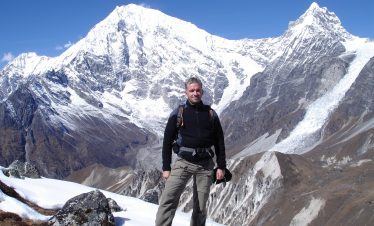 Trekker walking through Langtang Valley with panoramic views of snow-covered peaks and Kyanjin Gompa monastery in the distance