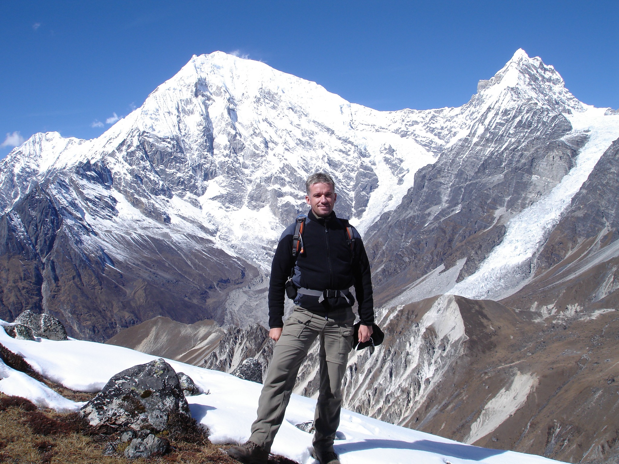 Trekker walking through Langtang Valley with panoramic views of snow-covered peaks and Kyanjin Gompa monastery in the distance