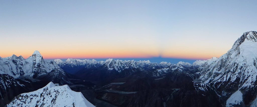 Mountaineer standing on Island Peak summit with panoramic view of Mount Everest and surrounding Himalayan peaks in Nepal.