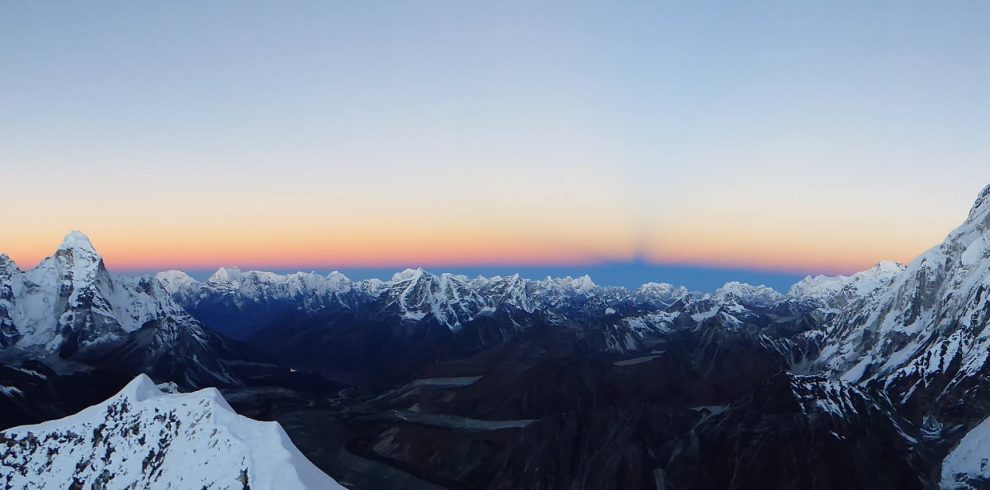 Mountaineer standing on Island Peak summit with panoramic view of Mount Everest and surrounding Himalayan peaks in Nepal.