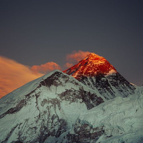 Spectacular view of Mount Everest at sunset with glowing red peak and dramatic sky.