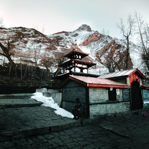 Exterior of aged abandoned house located near snowy slope of hill against cloudy gray sky