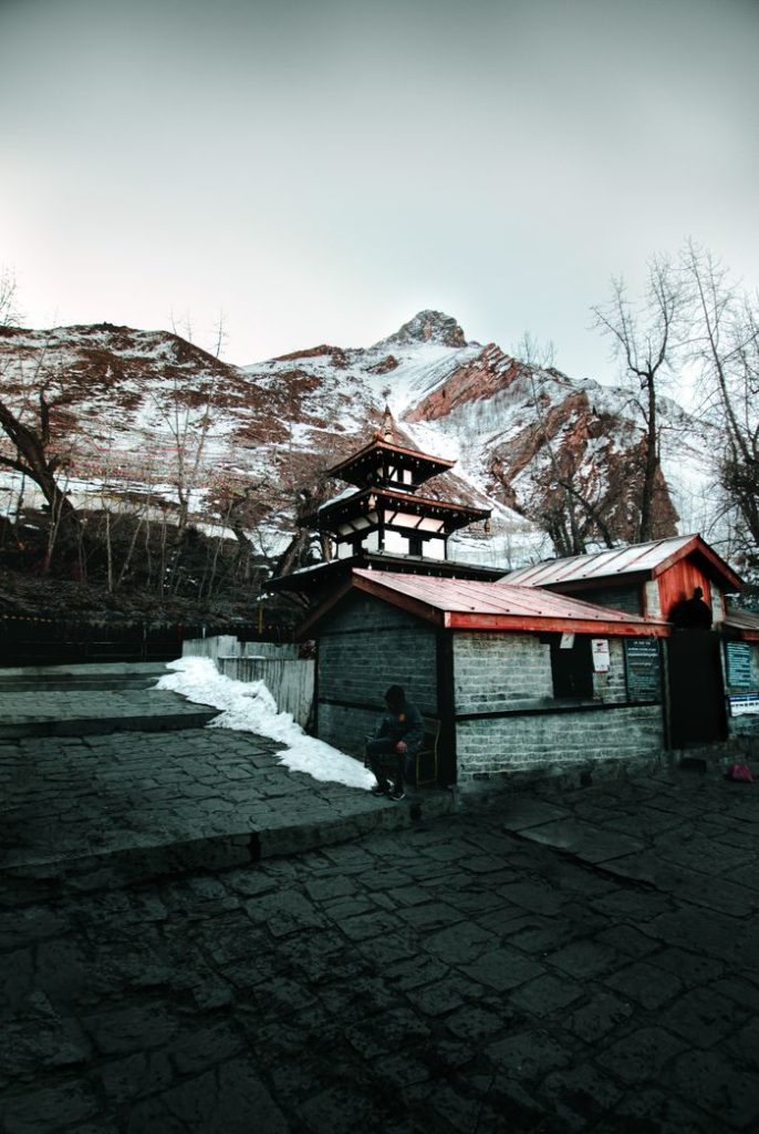 Exterior of aged abandoned house located near snowy slope of hill against cloudy gray sky