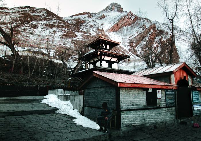 Exterior of aged abandoned house located near snowy slope of hill against cloudy gray sky