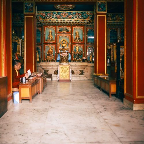 Interior of a Buddhist temple showcasing religious icons and a man sitting beside a donation box.