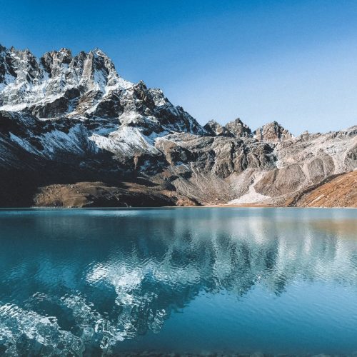 Breathtaking view of snow-capped mountains reflected in a serene blue lake in Nepal.