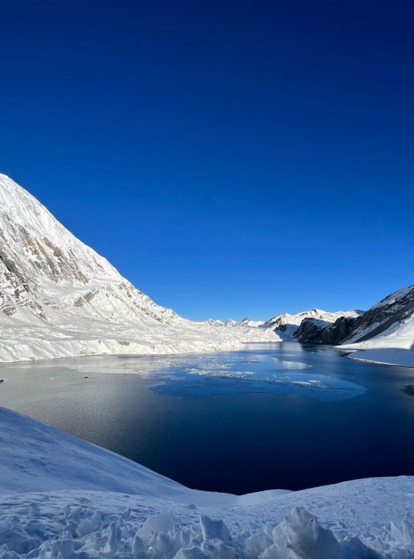 Breathtaking winter scene of a snowy alpine landscape with a tranquil lake and clear blue sky.