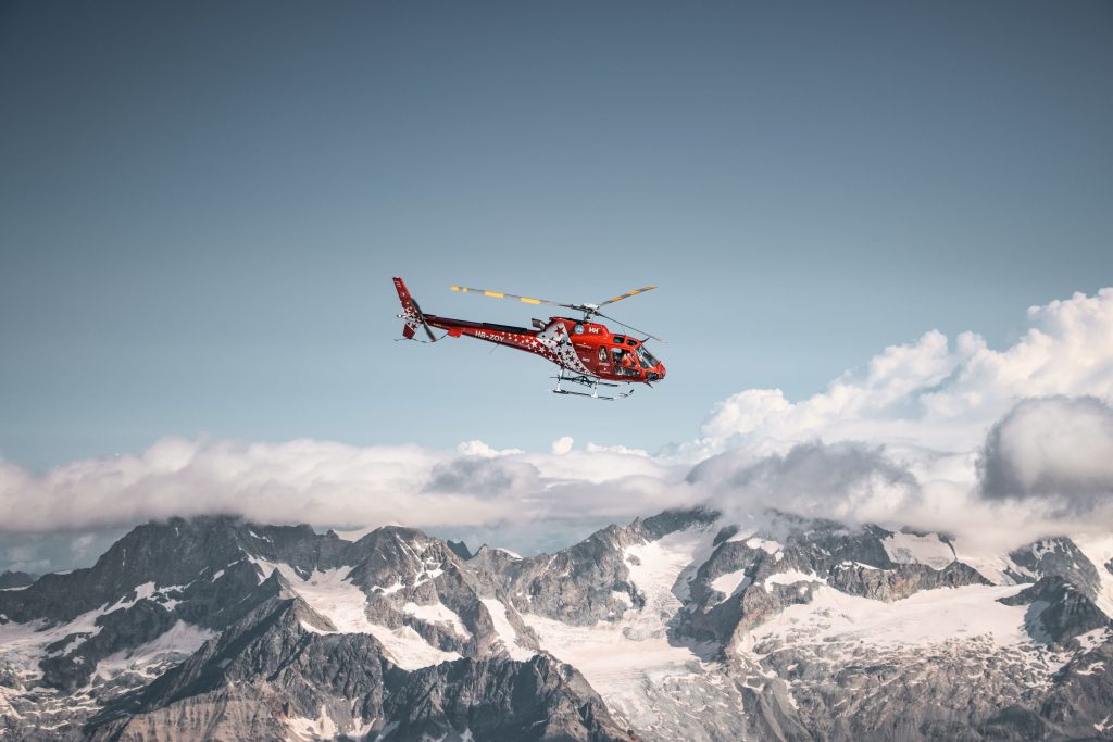 A vibrant red helicopter flies over the snowy peaks of the Swiss Alps, capturing a winter adventure.