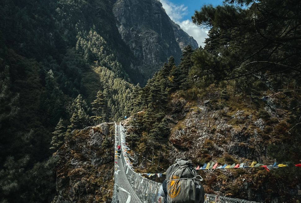 A hiker crosses a suspension bridge surrounded by stunning Himalayan views in Namche, Nepal.