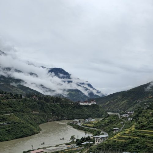 A breathtaking view of Wangdue Phodrang's lush greenery and river under cloud-kissed mountains.