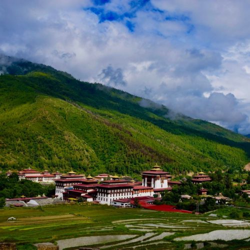 A breathtaking view of the Tashichho Dzong in Thimphu valley, surrounded by lush green mountains under a cloudy sky.