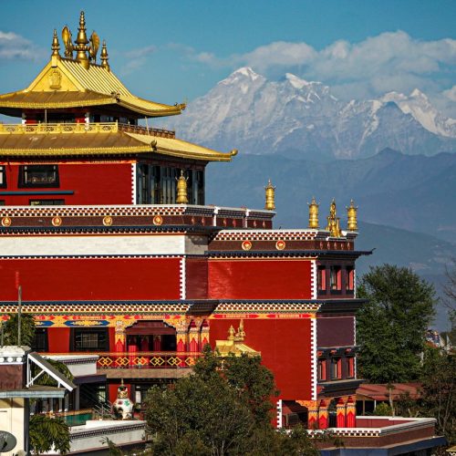 A vibrant golden-roofed temple set against the dramatic Himalayas under a clear blue sky.