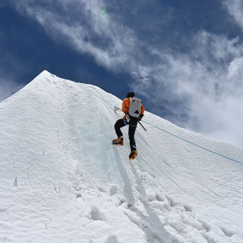 A climber ascends a snowy mountain peak in Nepal, showcasing adventure and perseverance.