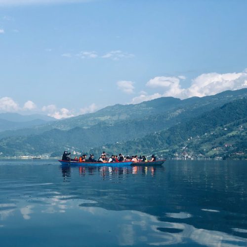 A group of people enjoying a boat ride on a serene mountain lake under a clear blue sky.